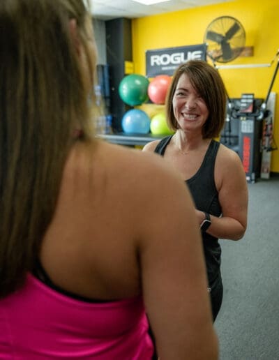 Personal trainer engaging with a client in a fitness studio, featuring exercise equipment and colorful stability balls in the background, emphasizing a supportive training environment.