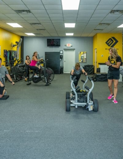 Group fitness session at Bill Cunningham Fitness, featuring clients engaging in strength training exercises with a sled and stationary bikes, guided by a personal trainer.