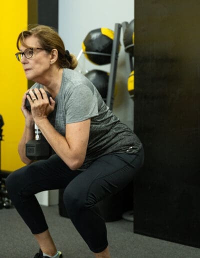 Woman performing a squat with a dumbbell in a fitness studio, emphasizing strength training and mobility, aligned with personal training services at Bill Cunningham Fitness.