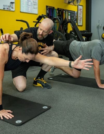 Personal trainer assisting a client with a strength training exercise in a fitness studio, emphasizing mobility and conditioning.